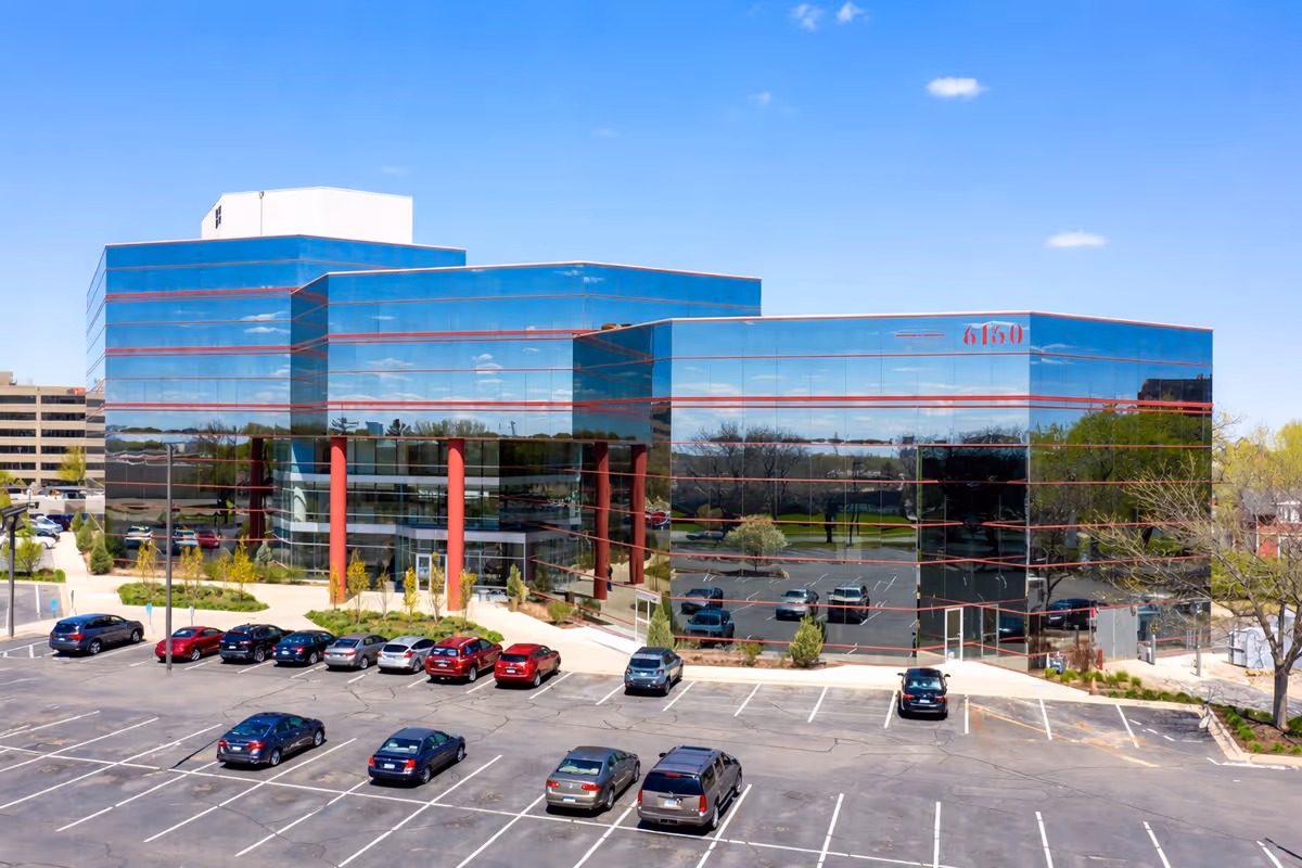 Glass-front building with red columns, blue-tinted windows, and a large parking lot.