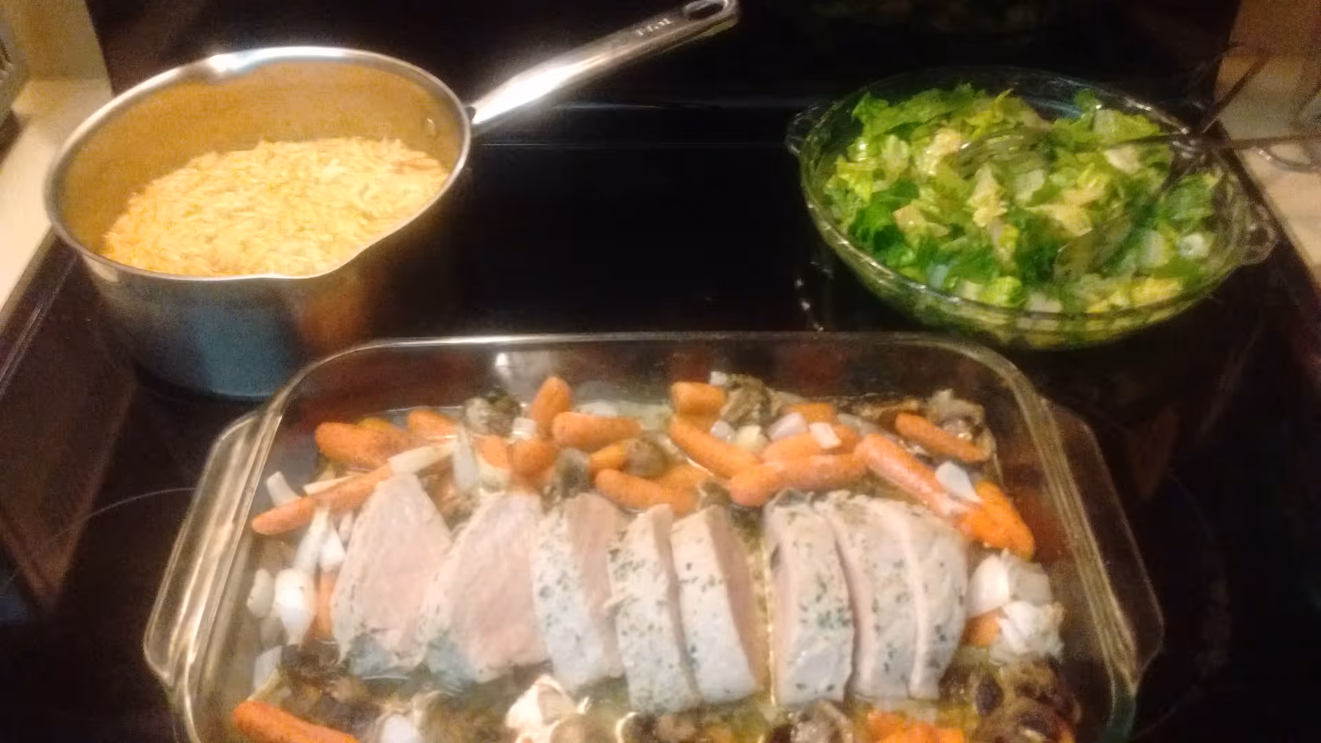 Rice pot, salad bowl, and sliced meat with carrots on the stovetop.
