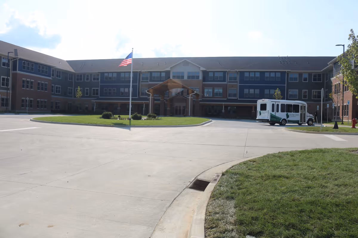 Exterior view of the Heritage Woods of Newburgh senior living facility with a flagpole and shuttle bus.