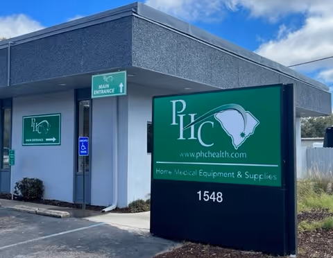 Front exterior of a PHC Health facility with large green sign near entrance.