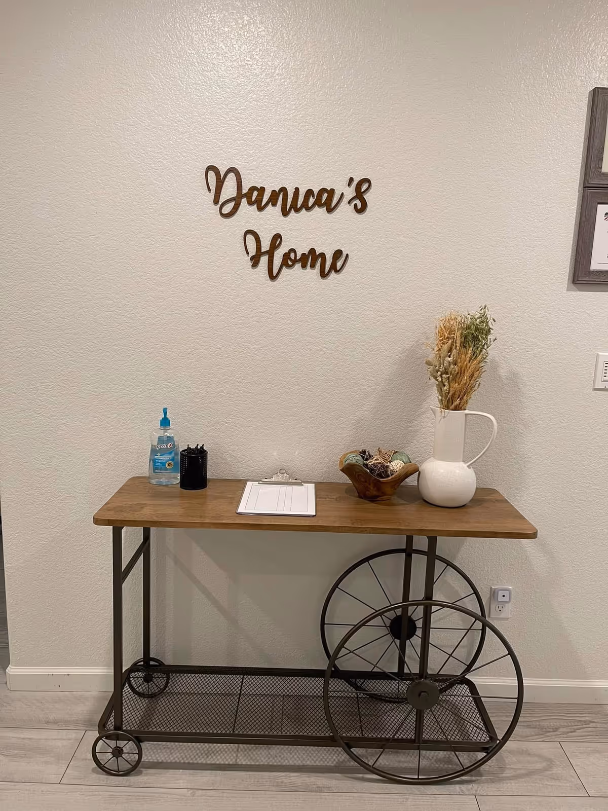 A wooden cart against a beige wall with Danica's Home sign and decor.