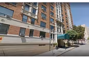 Brick senior living building with green awning entrance along a sunny city sidewalk.