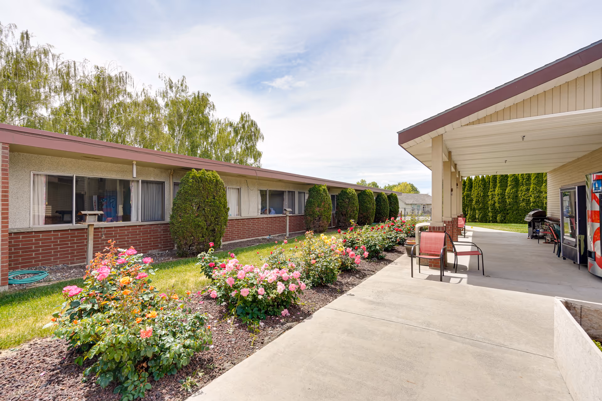 Exterior view of a single-story senior facility with rose beds and a covered entrance.