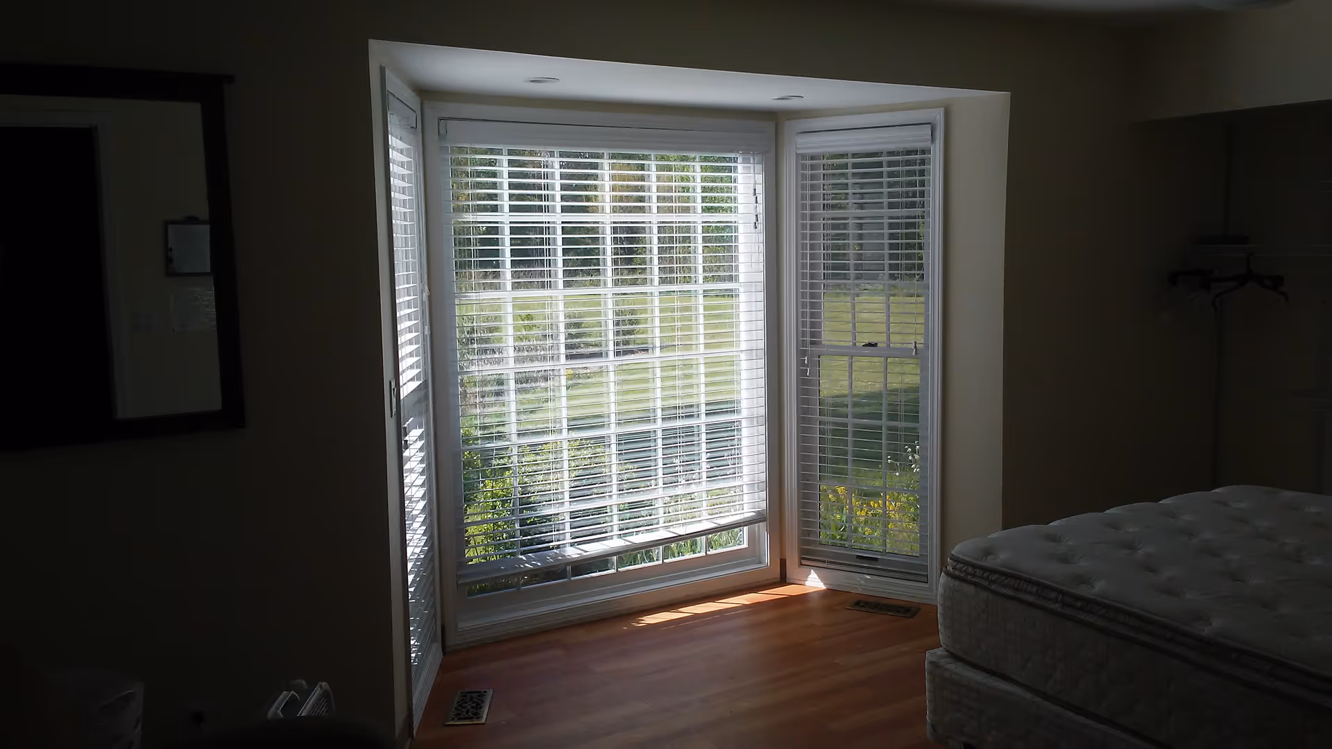 Bright bedroom with a bay window, blinds, and a mattress on a bed frame.