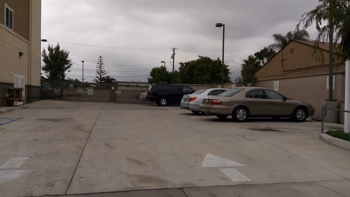 Exterior parking lot at Normandie Senior Housing, with cars, gate, and cloudy sky.