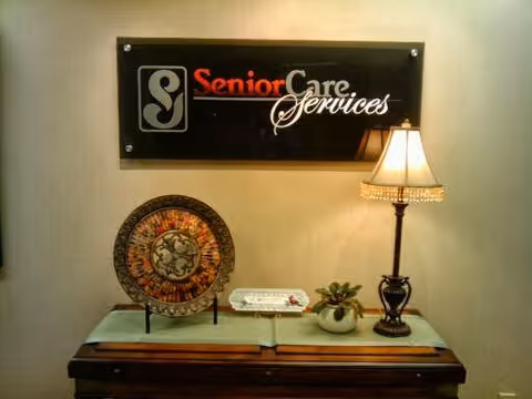 Interior desk area with a Senior Care Services sign, lamp, decorative plate, and plant.