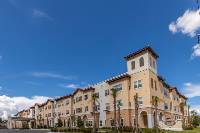 Exterior view of Palagio Senior Living building with arches and palm trees.