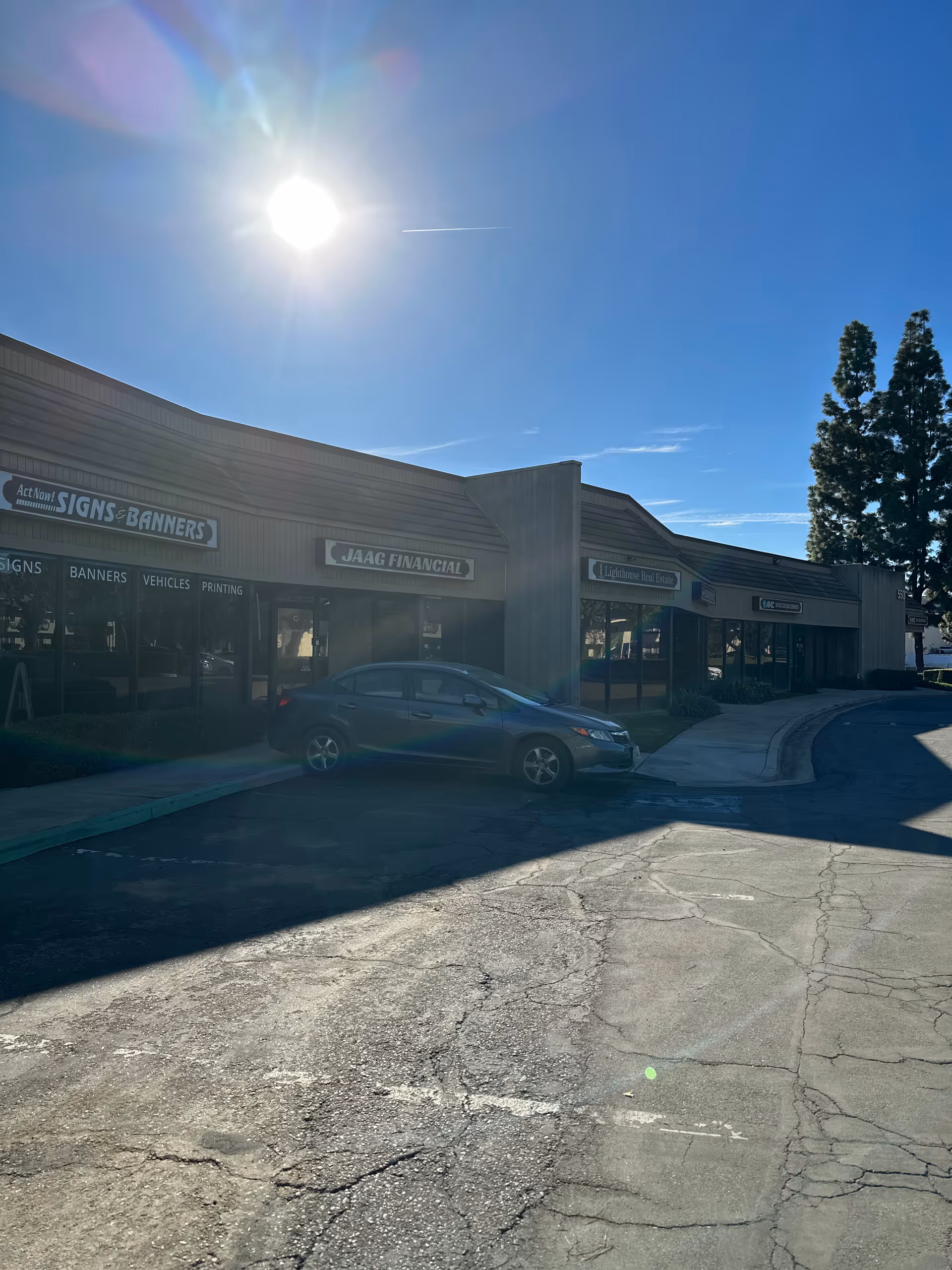Sunny parking lot in front of storefronts with a parked car.