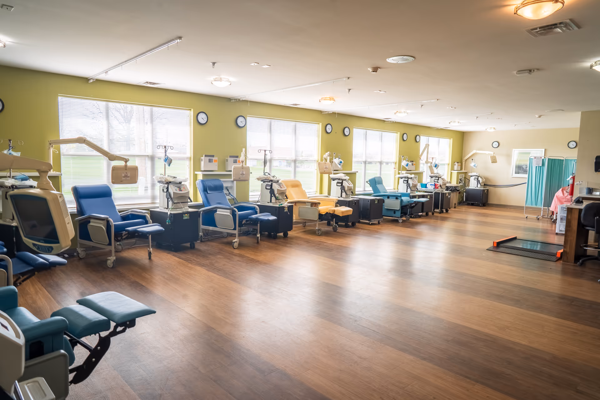 A long treatment room with multiple reclining chairs, machines, and windows along lime-green walls.