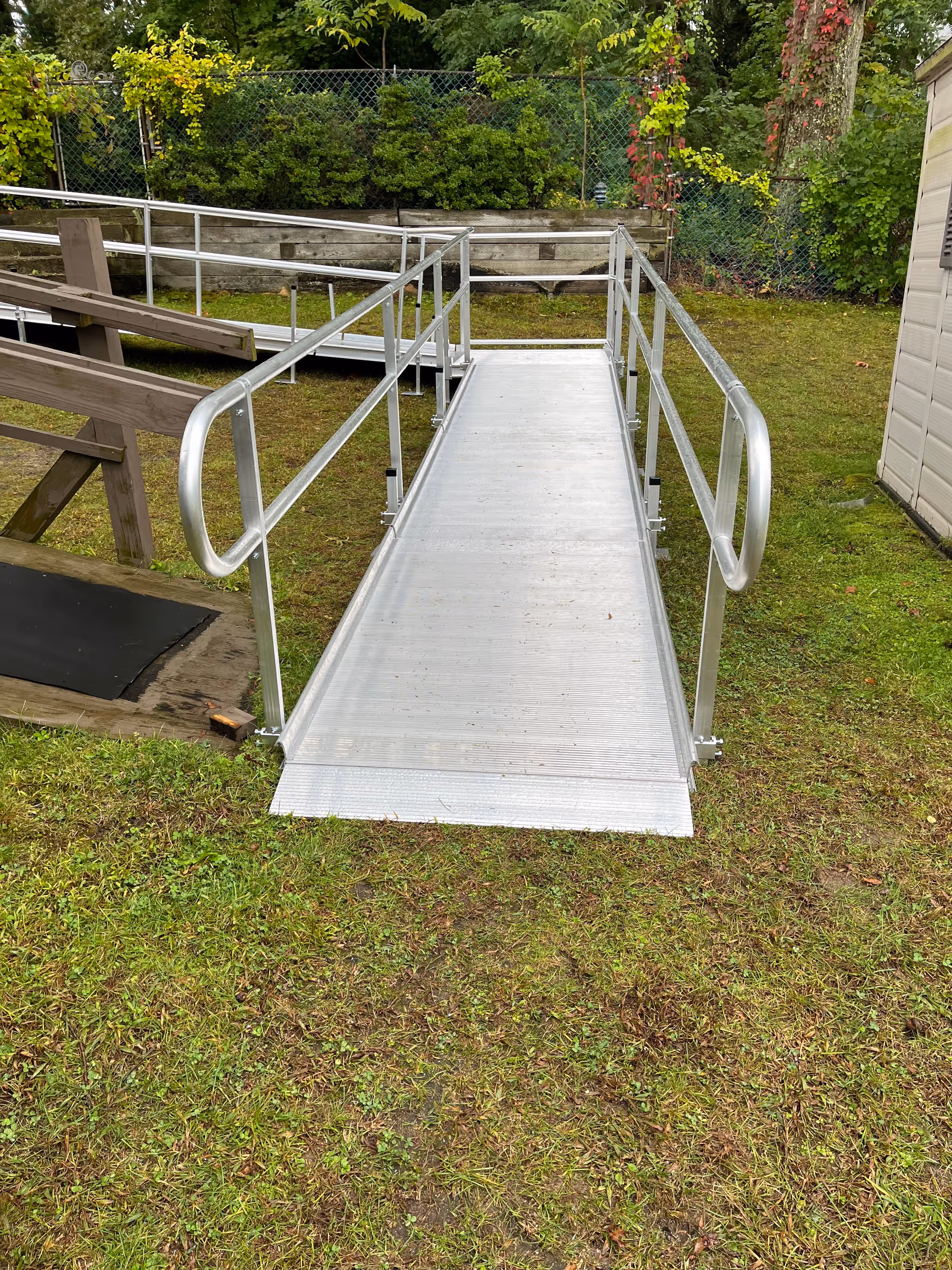 Metal wheelchair ramp extends over grass toward a fenced outdoor area.