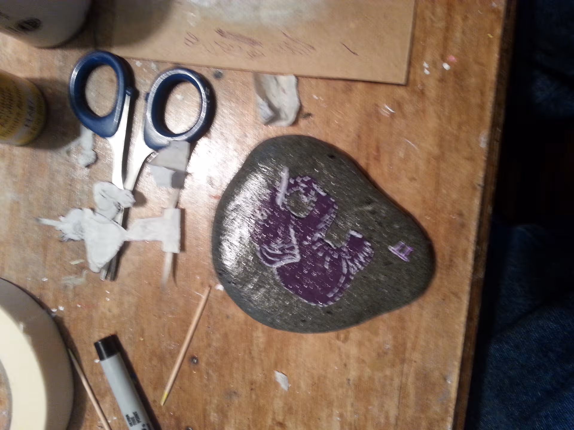 Close-up of a craft table with scissors, glue, and a painted rock.