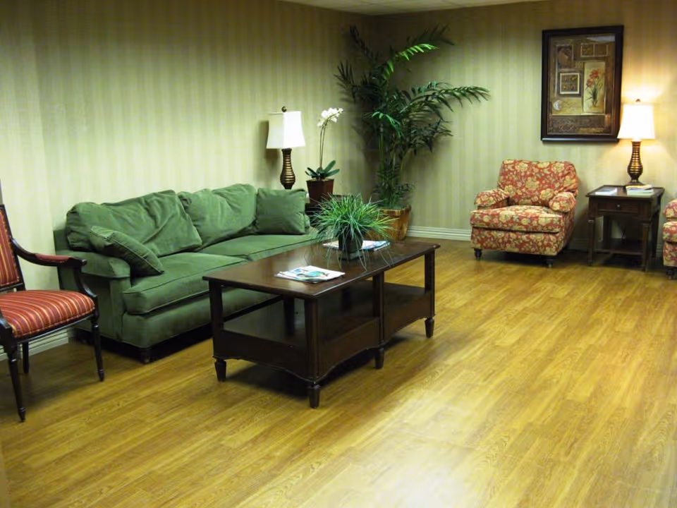 Cozy indoor lounge in a senior living facility featuring a green sofa, plants, and patterned chairs.