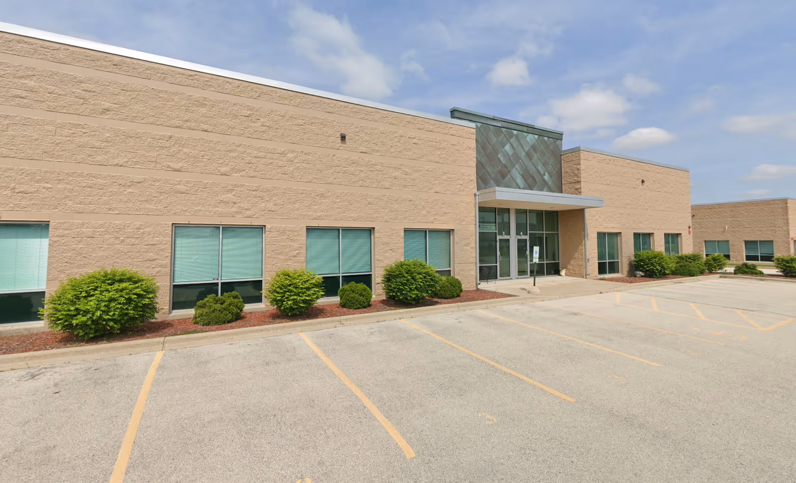 Exterior view of a beige senior living facility with glass entry and shrubs.