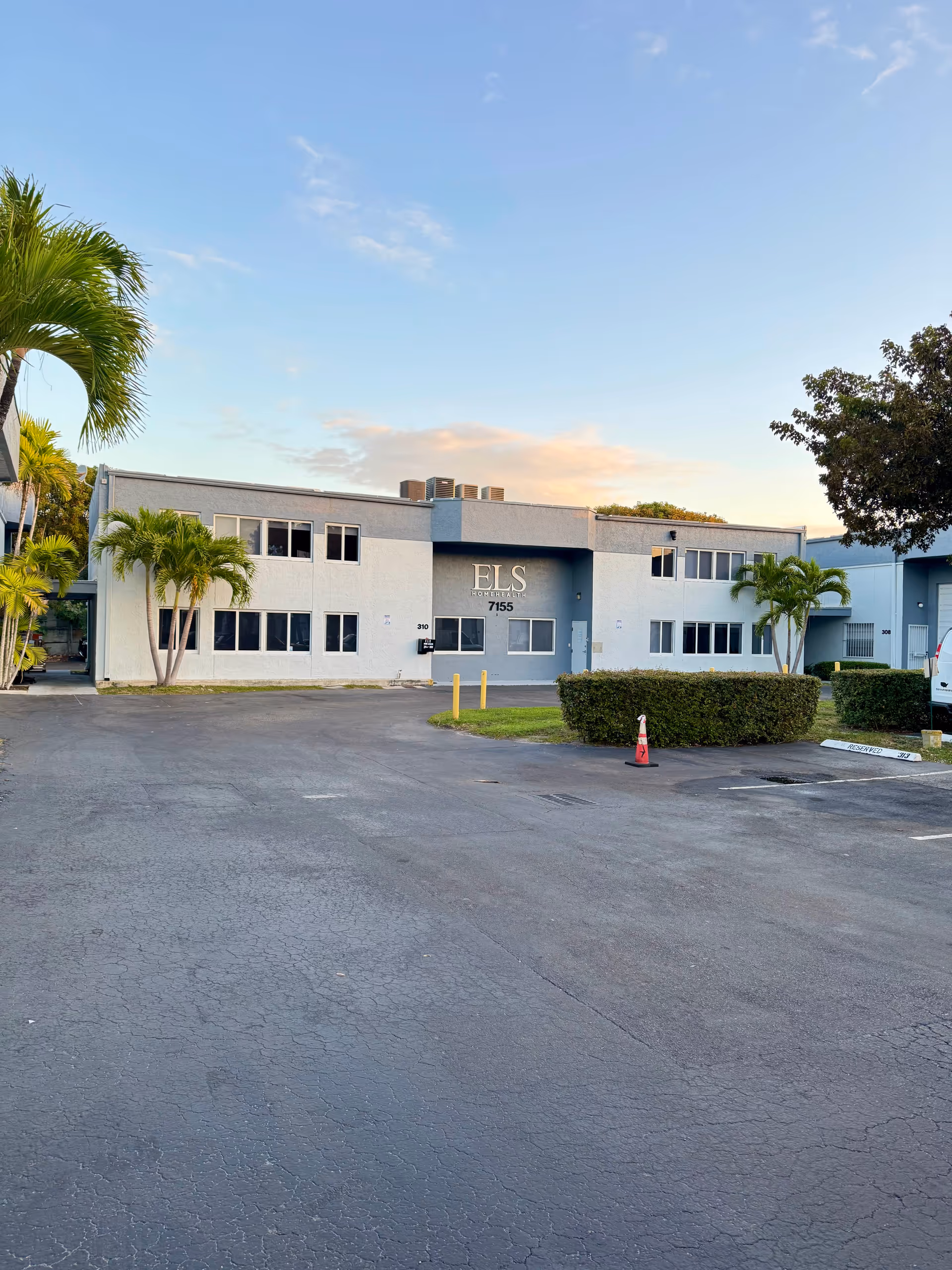 Two-story light-blue facility with ELS sign, parking lot, and palm trees outside.