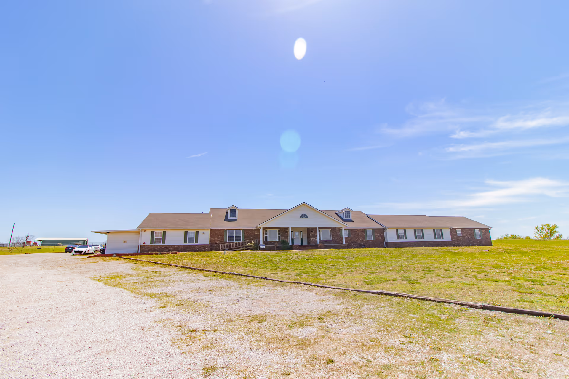 Single-story brick care facility with central front entrance, cars nearby, and vast lawn.
