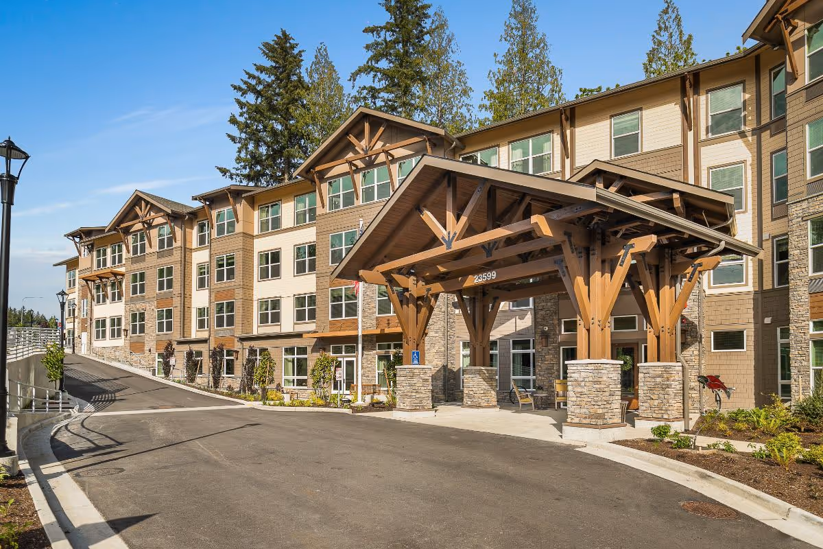 Exterior front entrance of a multi-story senior living building with a large wooden porte-cochère and driveway.