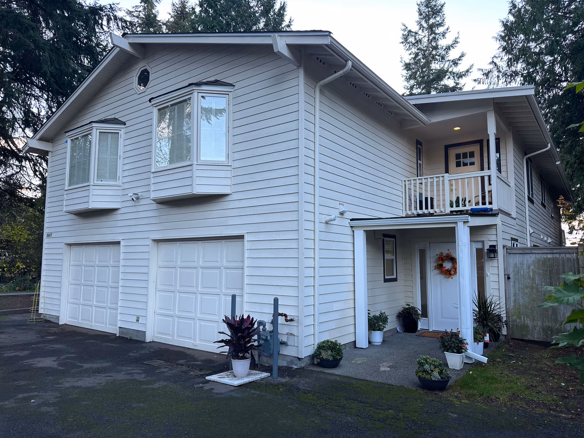 Two-story light-siding building with attached garage doors, a front porch, and potted plants.