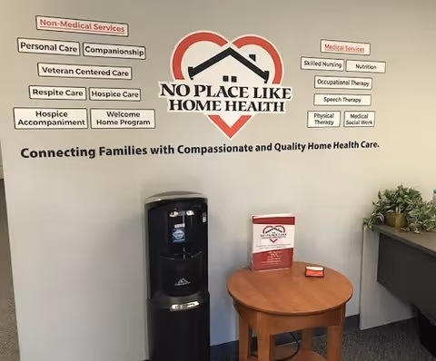 Interior wall displays No Place Like Home Health logo with service labels, water cooler, and table.
