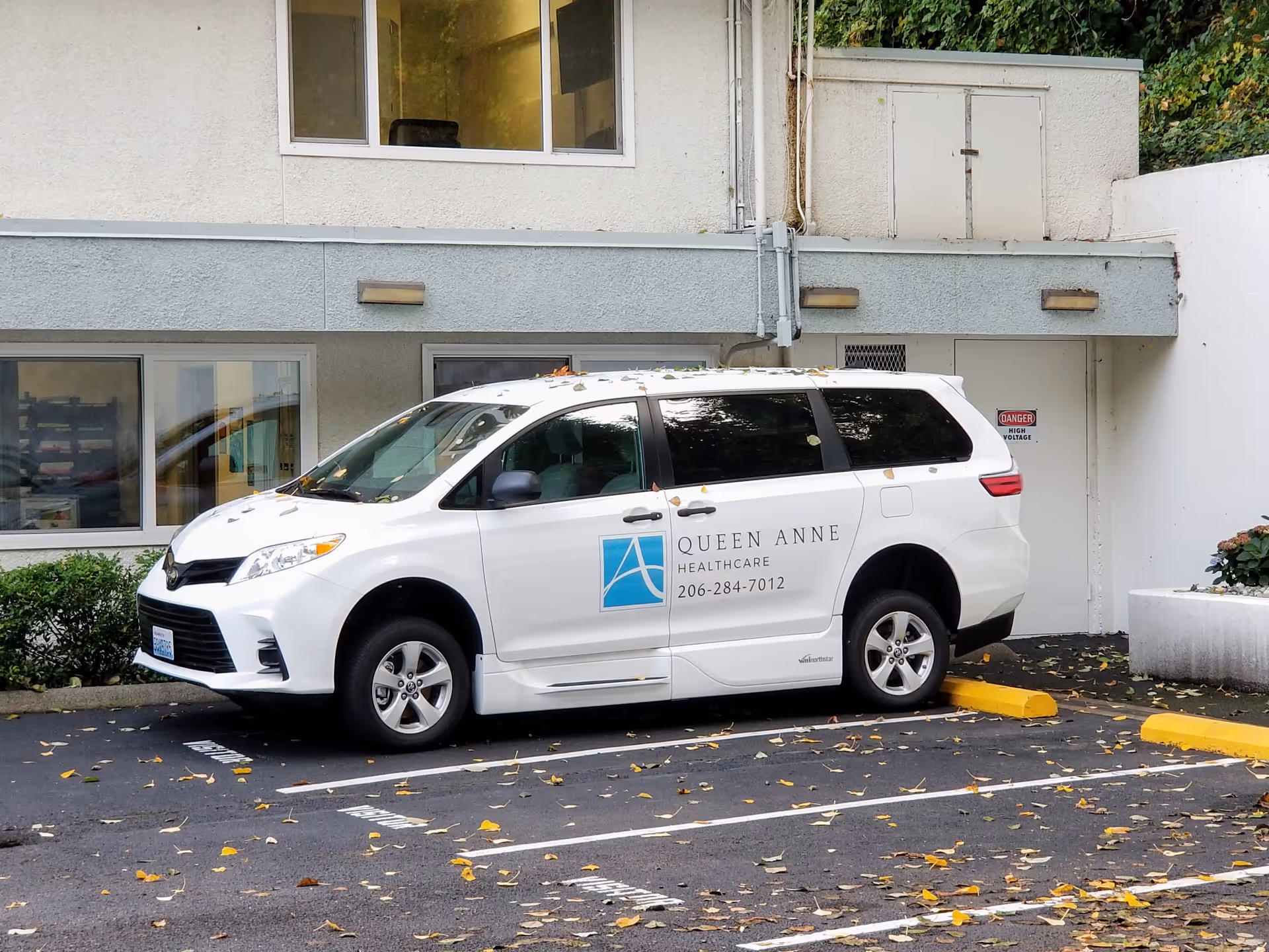 Queen Anne Healthcare van parked in front of a gray building.