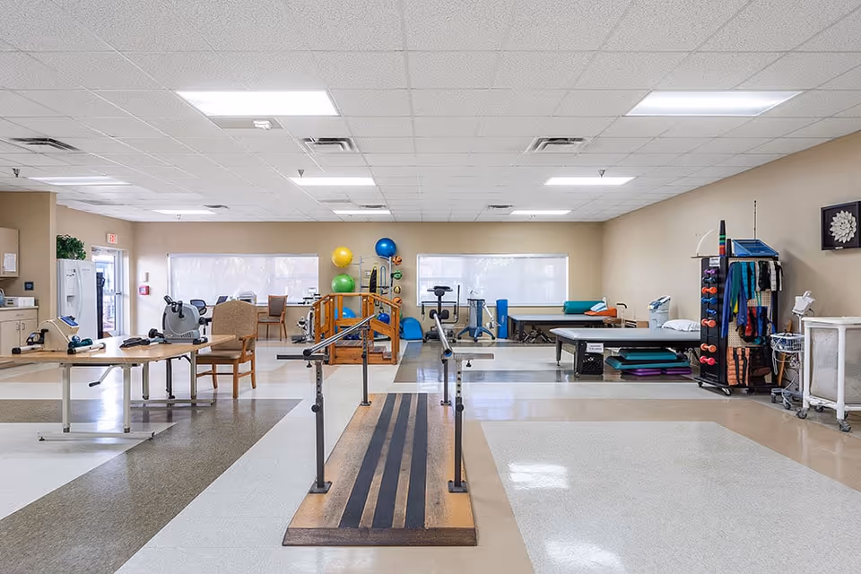 Spacious physical therapy room with parallel bars, exercise equipment, exercise balls, and treatment tables.