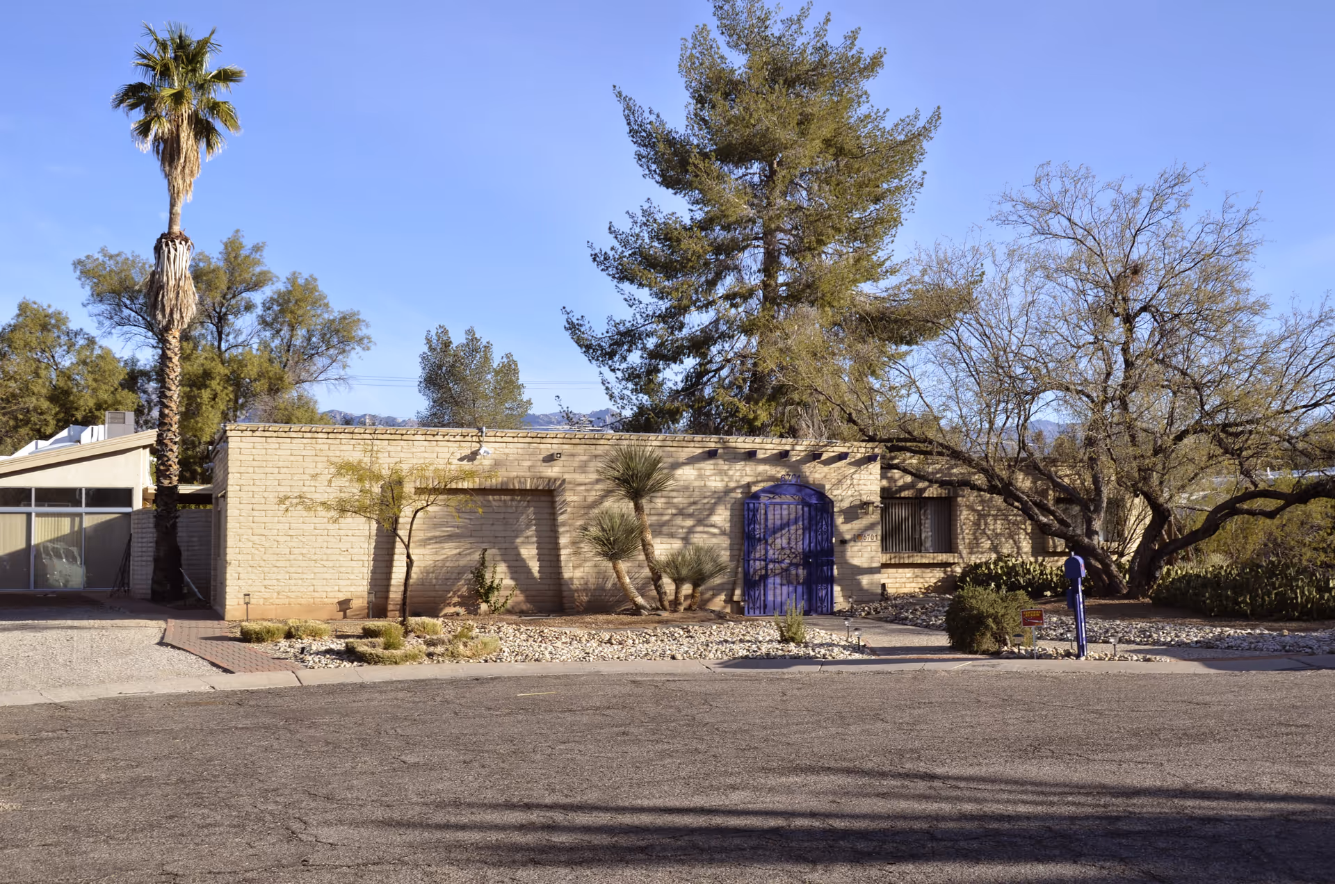 One-story beige brick facility exterior with purple gate, desert landscaping, and bare trees.