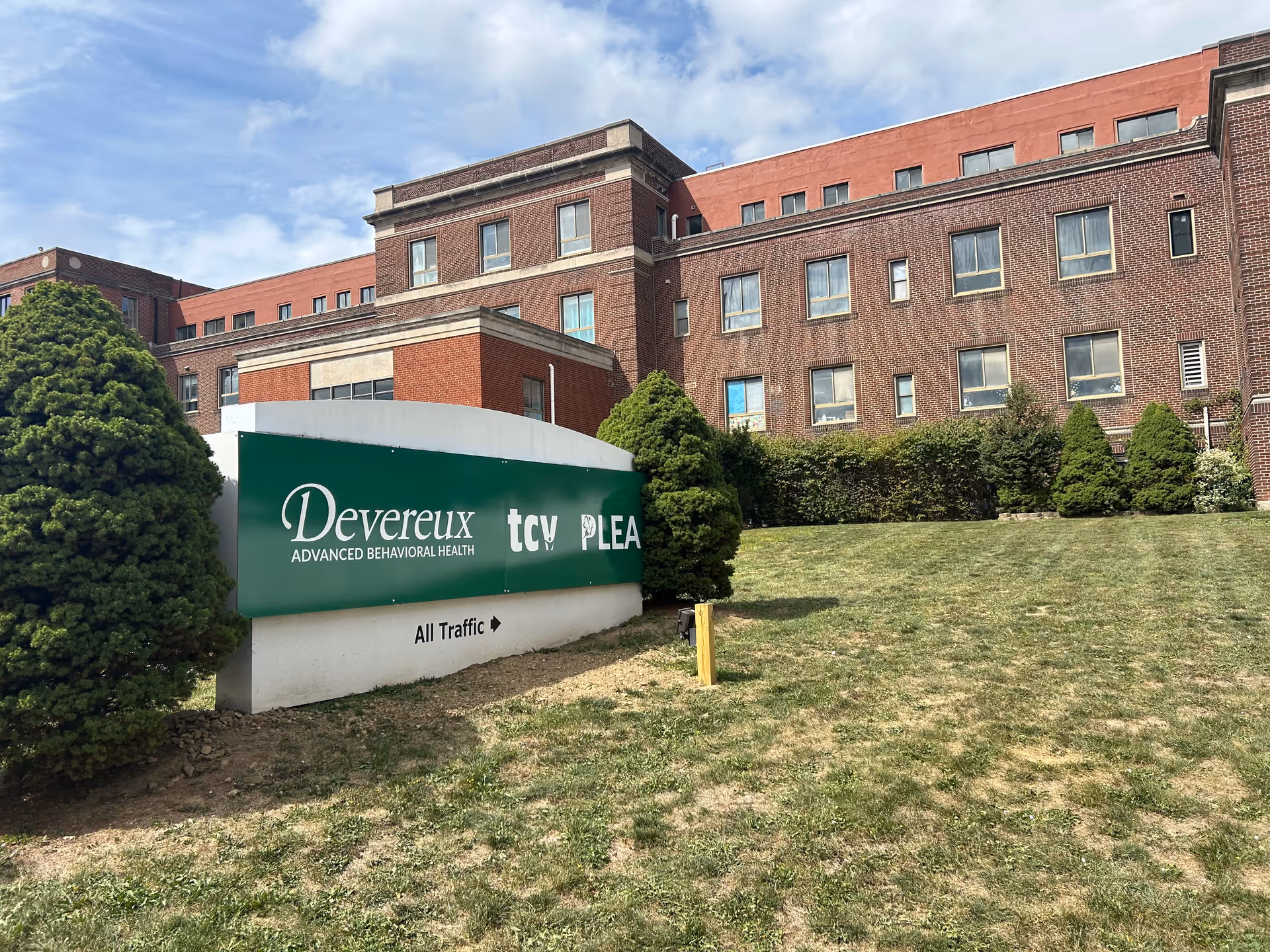 Exterior of a brick facility with a green sign and trimmed landscaping.