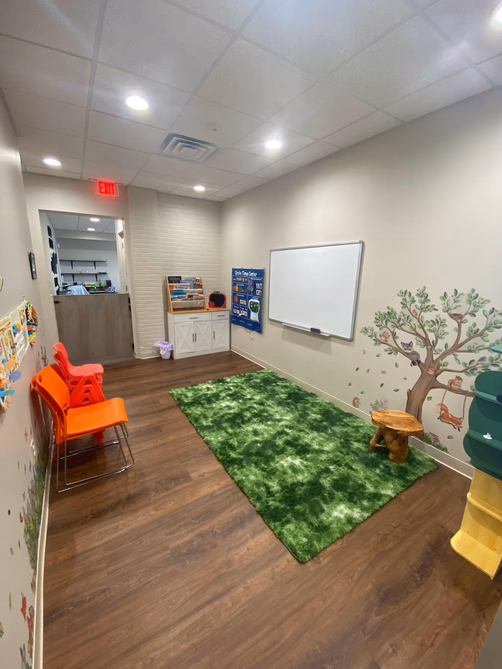 Senior living activity room with orange chairs, a whiteboard, and tree mural.