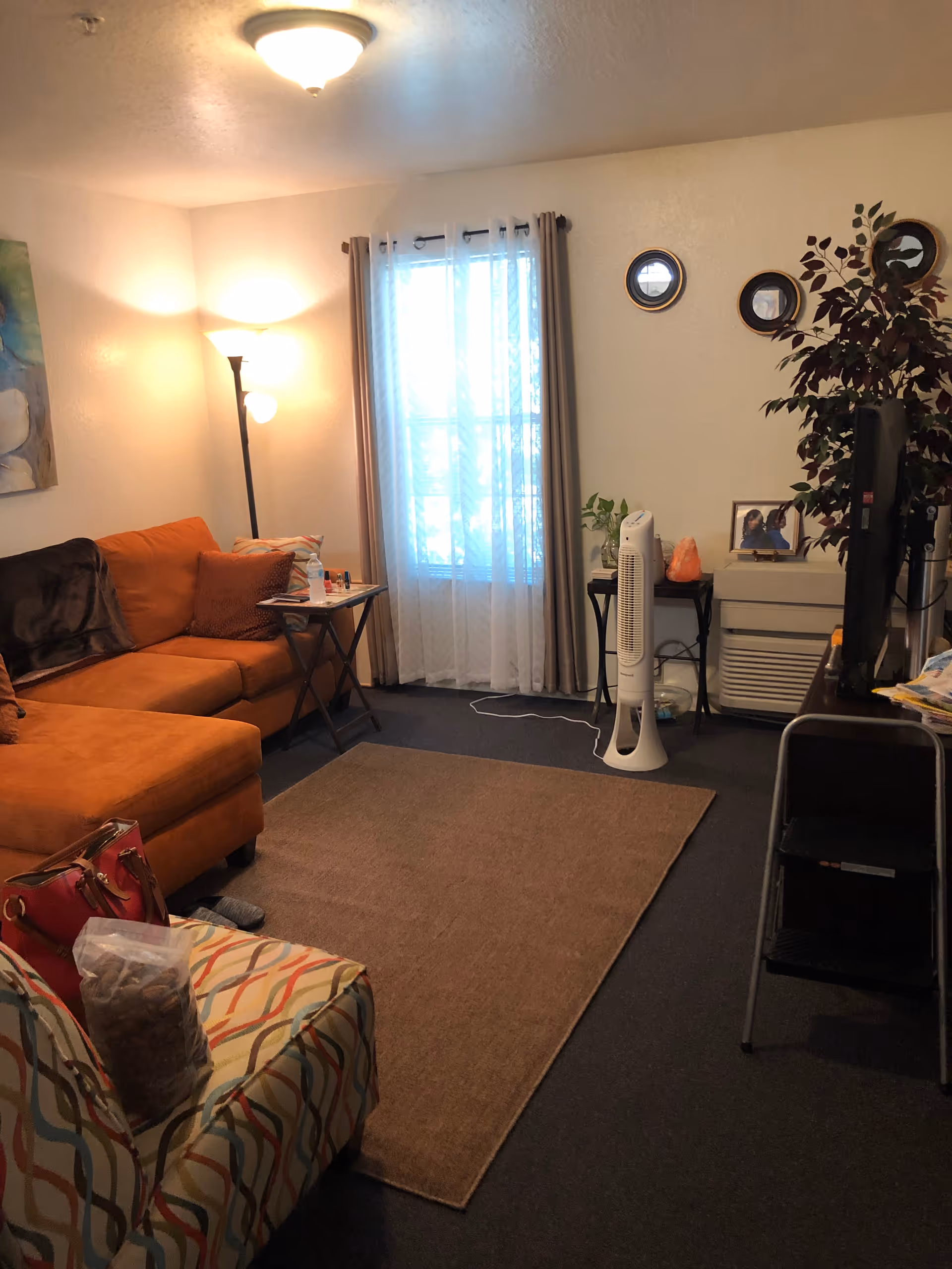 Cozy living room in senior housing with orange sofa, chair, rug, fan, and TV.