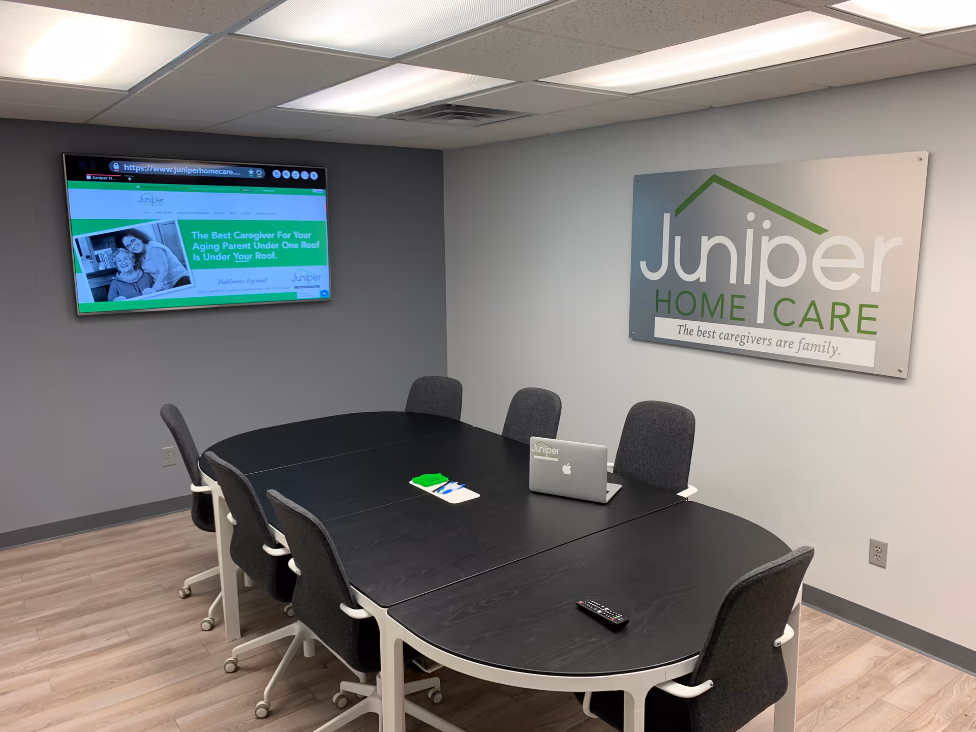 Modern conference room with a curved black table, laptops, and Juniper Home Care signage.