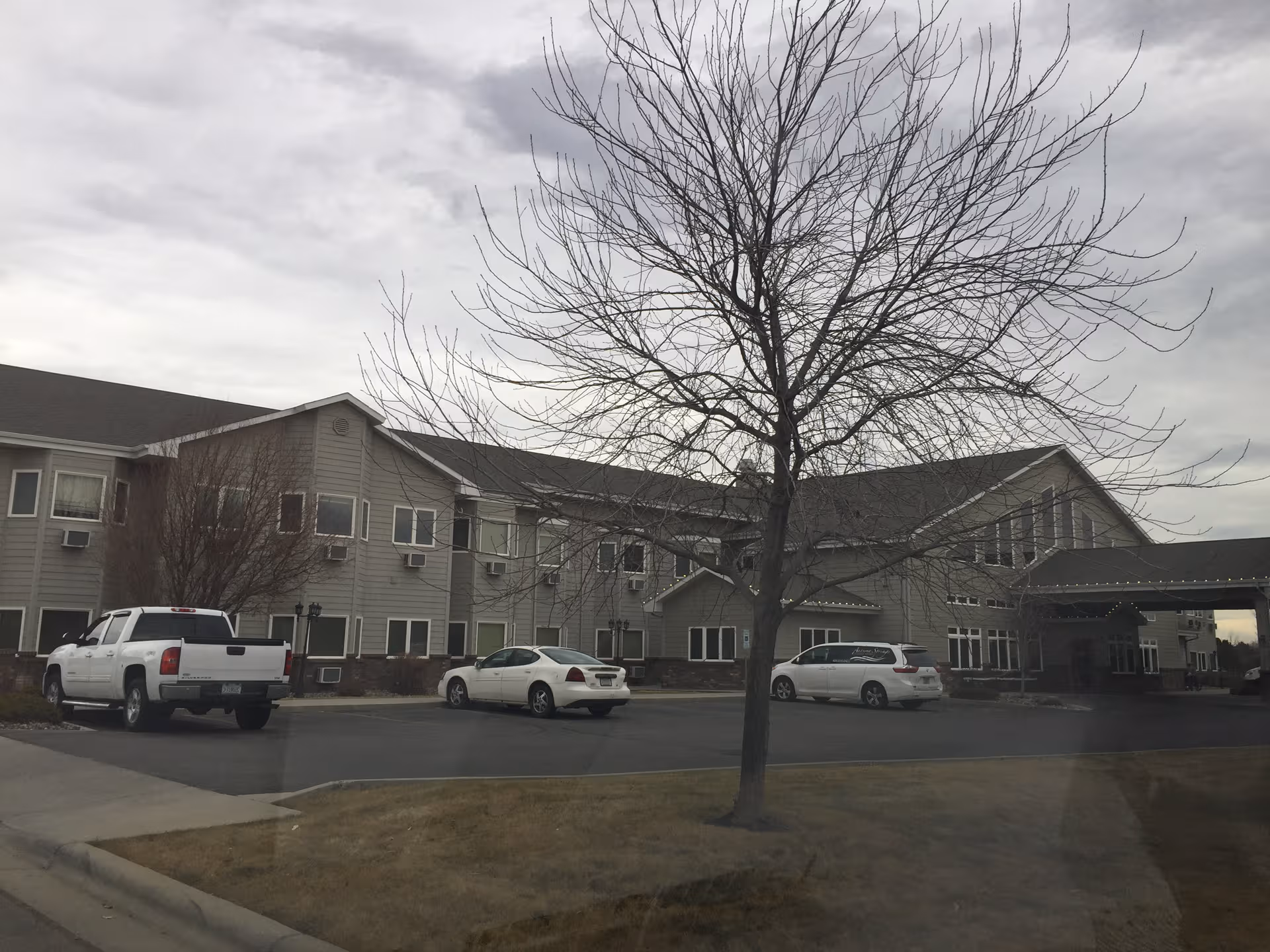 Exterior view of Autumn Springs Assisted Living building with parked cars and a bare tree.