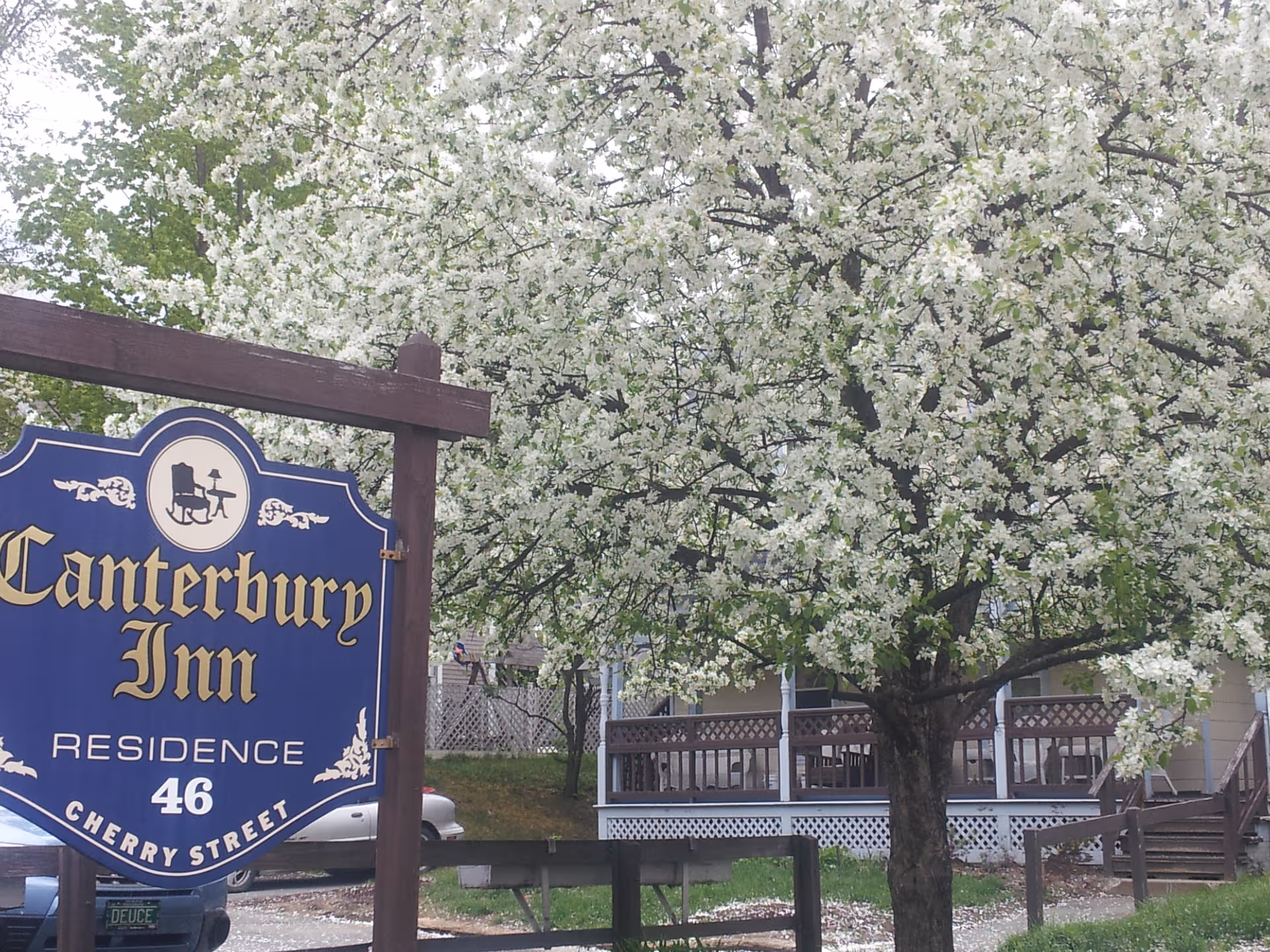 Blue Canterbury Inn sign beside blooming trees and a front porch residence.