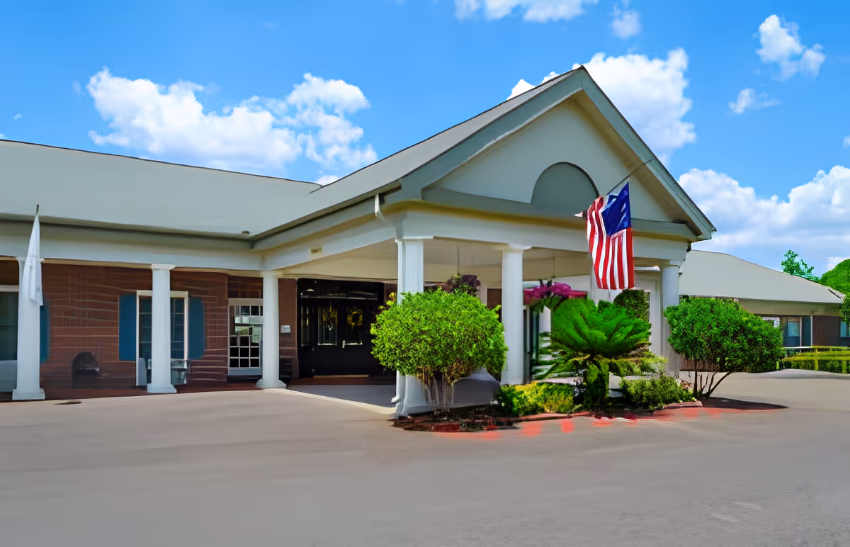Front entrance of a senior living facility with a columned portico, American flag, and landscaped driveway under a blue sky.