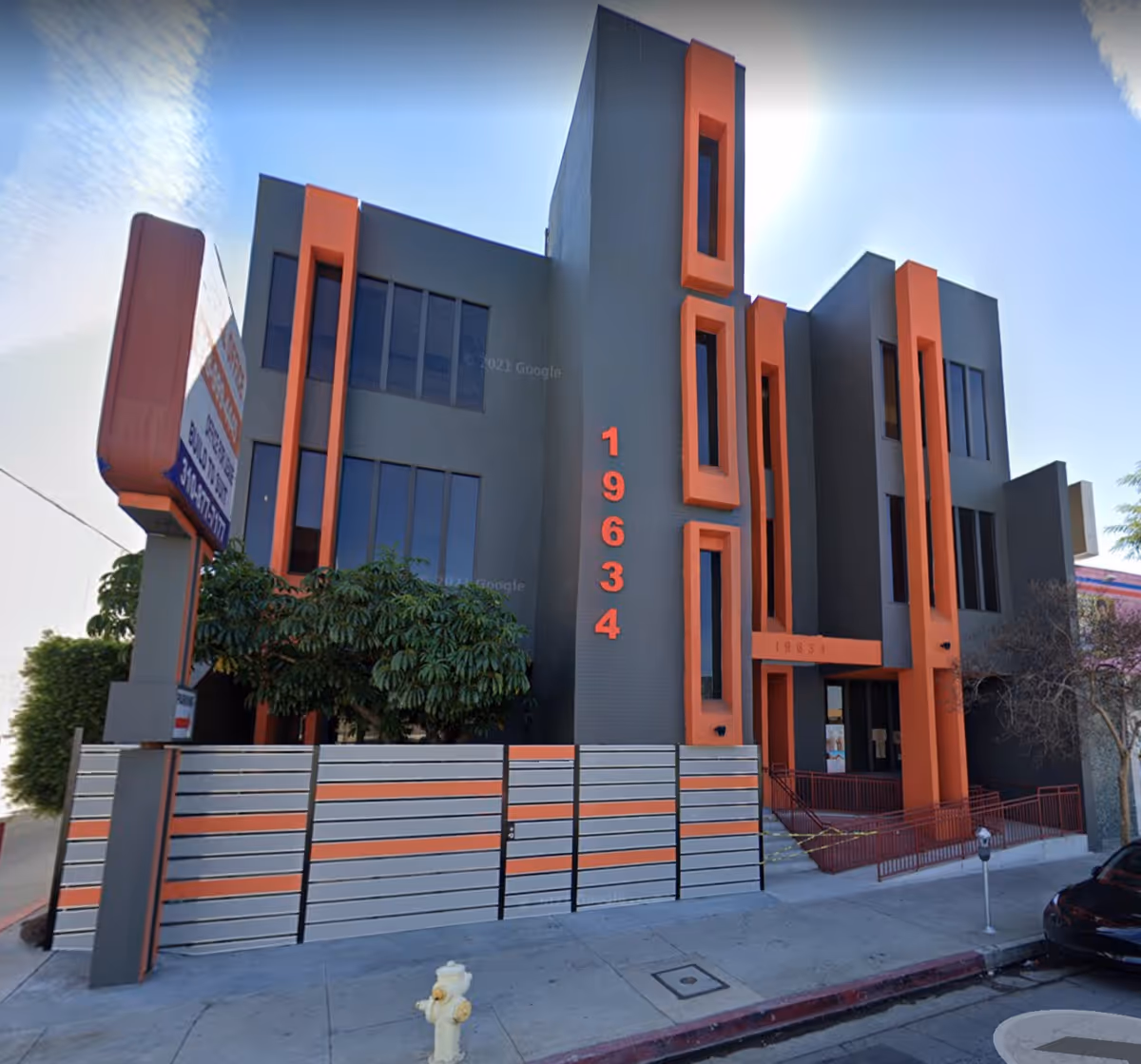 Modern gray and orange building facade with tall vertical window frames along the street.