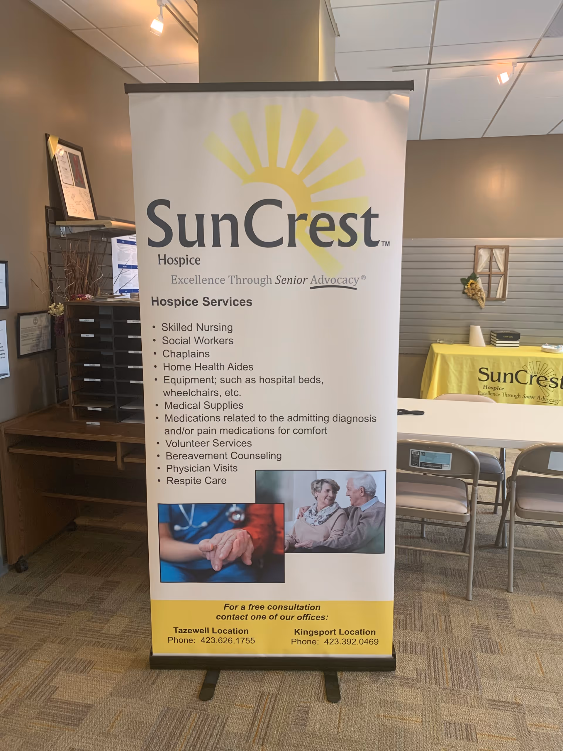 Tall SunCrest Hospice banner stands in a lobby with tables and chairs in view