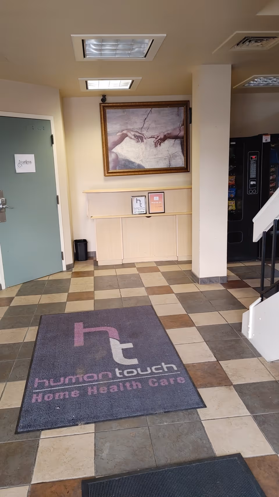 Interior lobby area with tiled floor, vending machine, framed artwork, beige cabinet, and a mat.