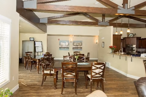 Open communal dining room with wooden tables and chairs, exposed wooden ceiling beams, and a kitchen counter with pendant lights.