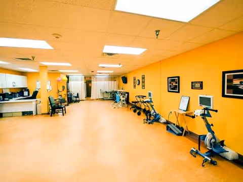 Bright orange-walled rehabilitation gym with exercise bikes and scattered seating inside the facility.