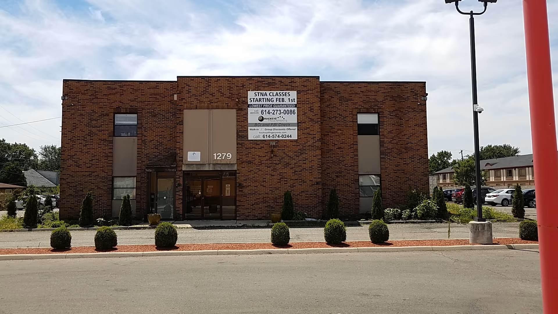 Brick building with glass doors, sparse landscaping, and a parking lot.