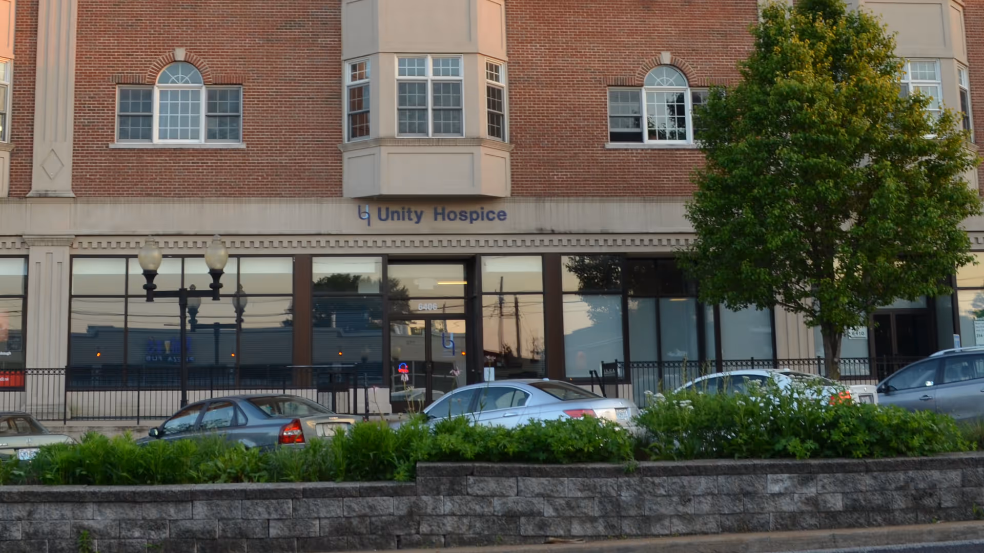 Brick storefront with Unity Hospice sign, large windows, and parked cars in front.