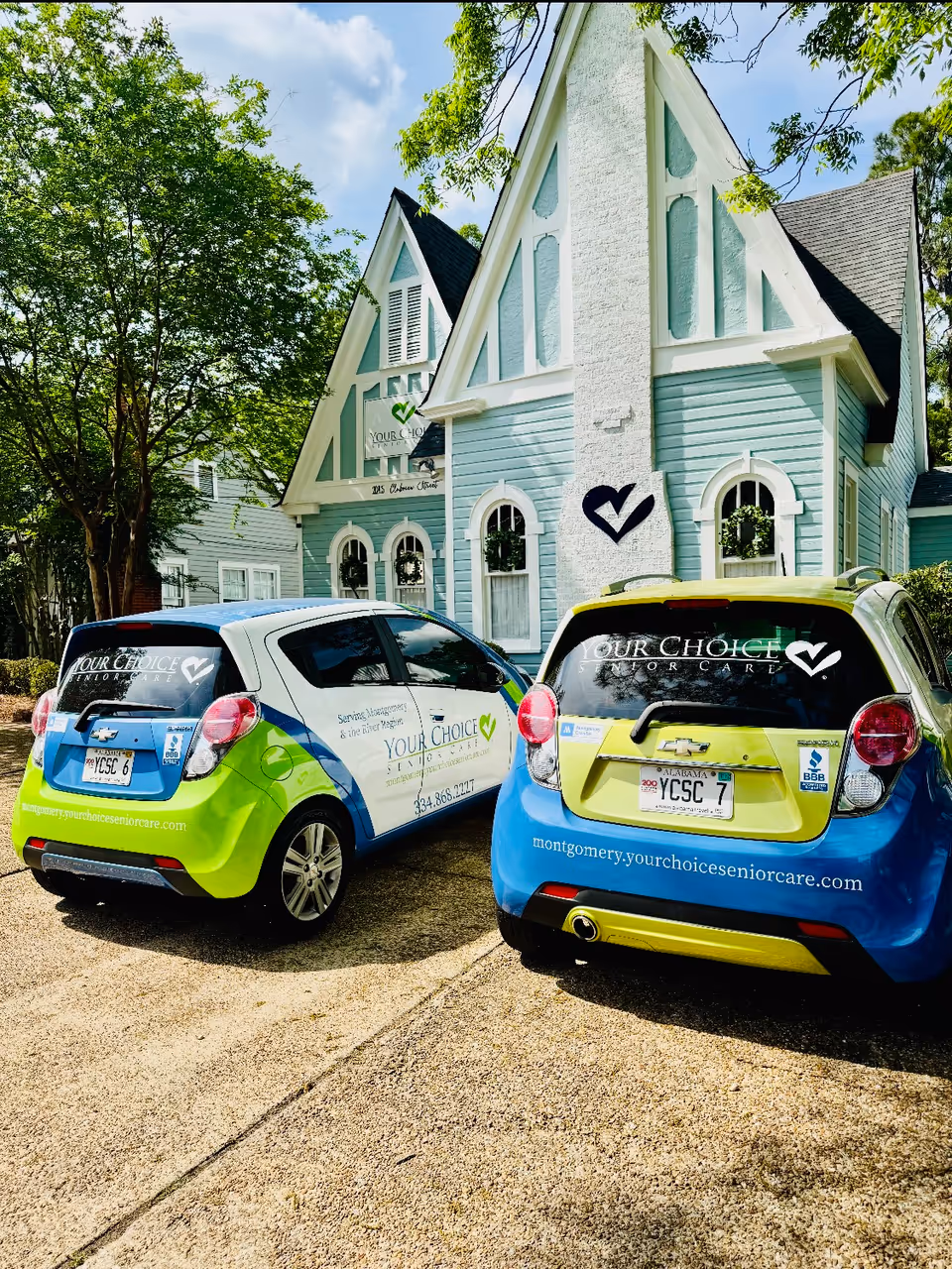 Two colorful Your Choice Senior Care vehicles parked before a light-blue building with a peaked roof.