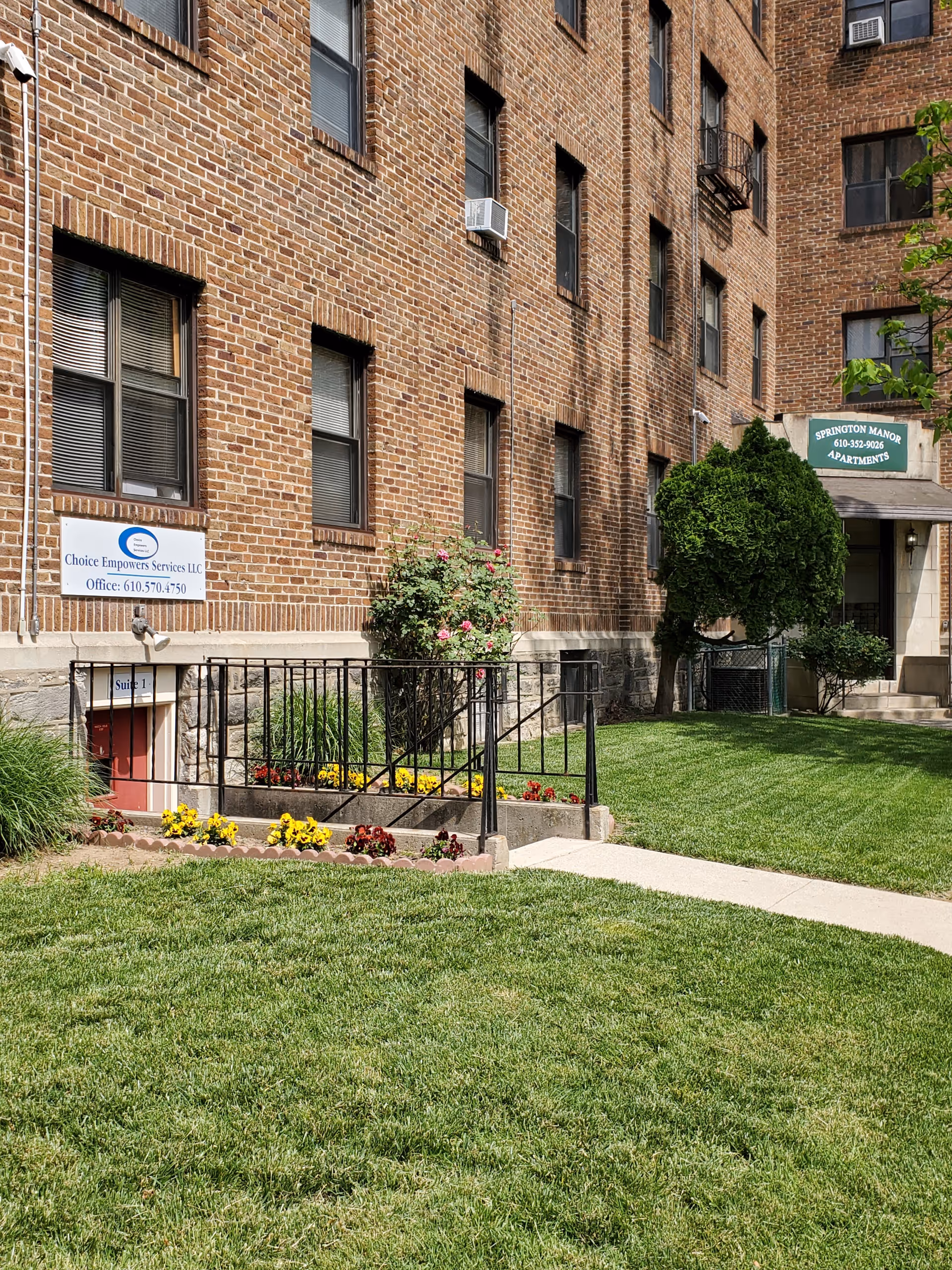 Brick apartment building entrance with ramp, signs, and manicured lawn.