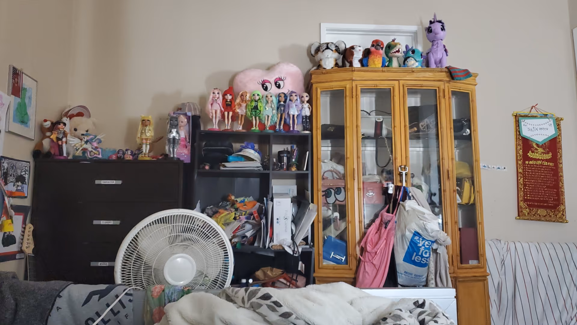 A cluttered indoor living area with toys on shelves and a glass-front cabinet.