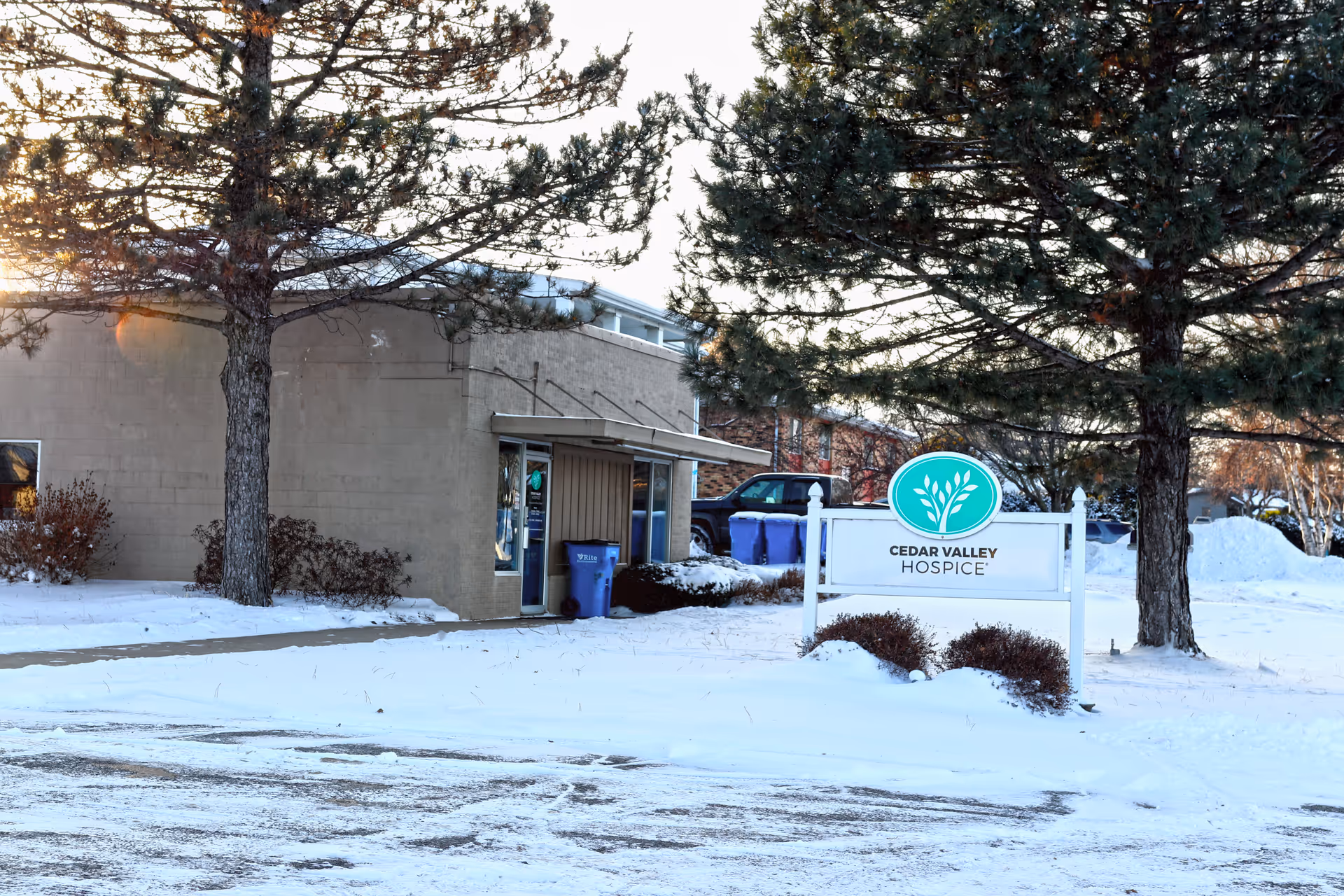 Snow blankets the exterior of Cedar Valley Hospice with a sign and trees.