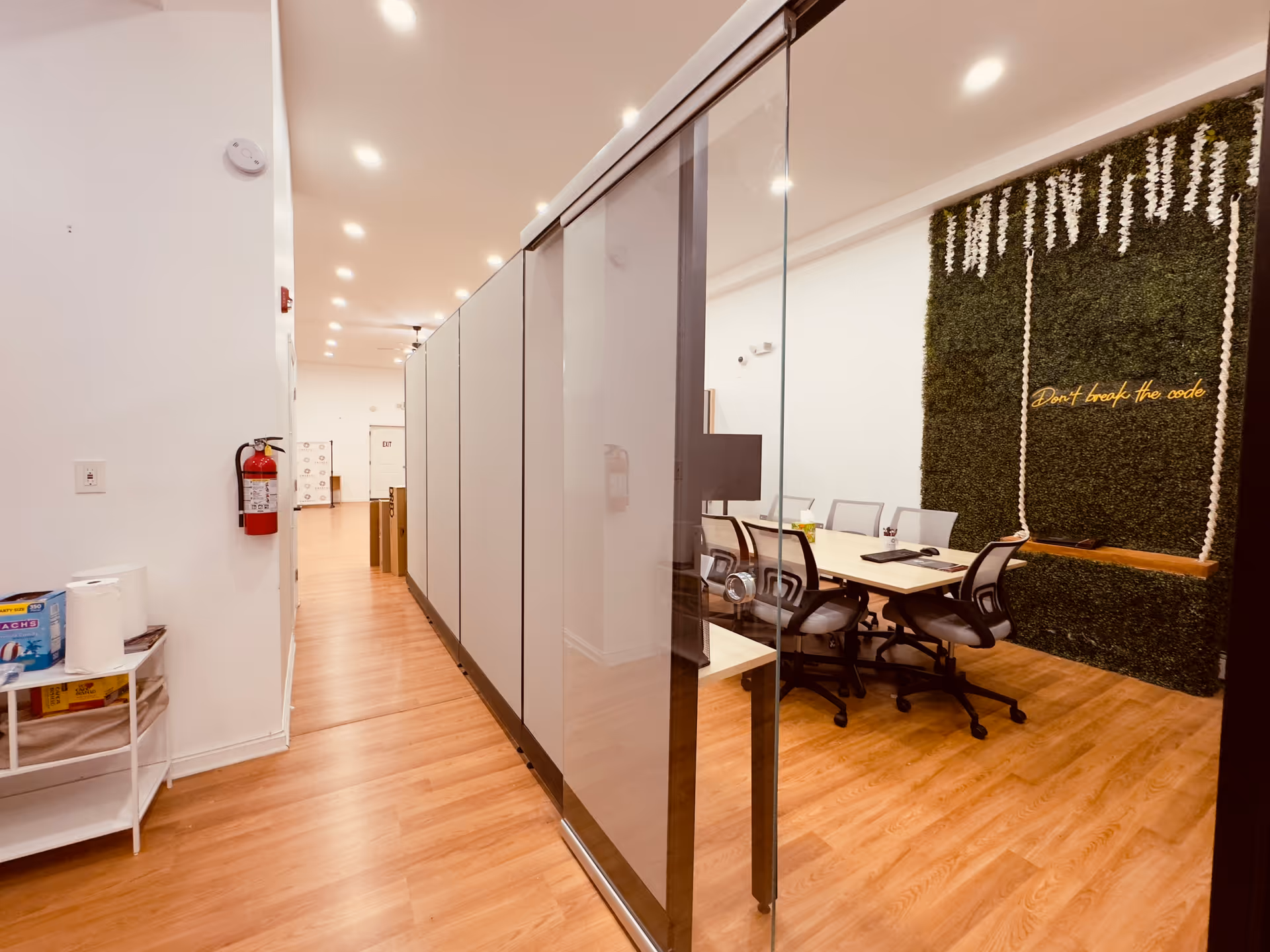 Glass-walled conference room along a hallway with a green decorative wall.