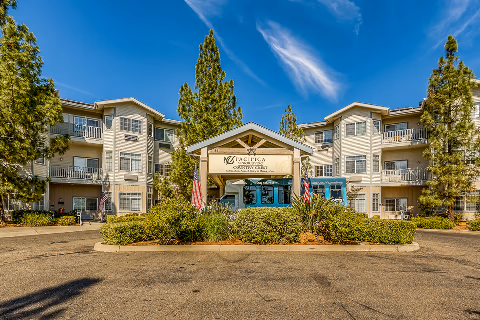 Front entrance of Country Crest Senior Living building with a covered porte-cochere, landscaping and American flags.