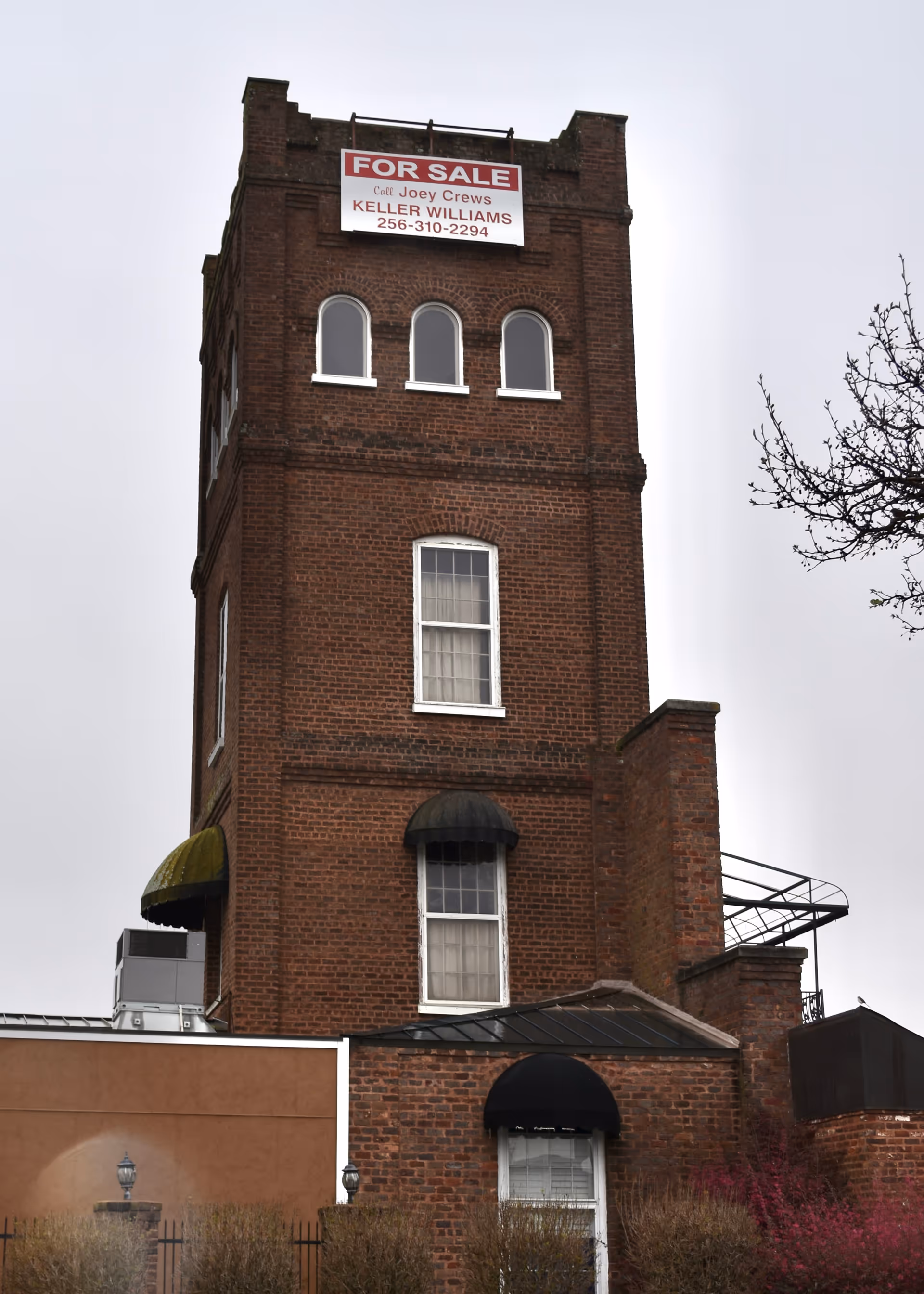 Tall red brick building with a FOR SALE sign on top.