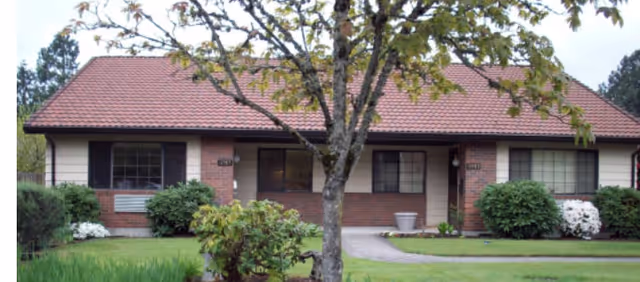 Front of a single-story brick senior living building with a red-tile roof and trees.