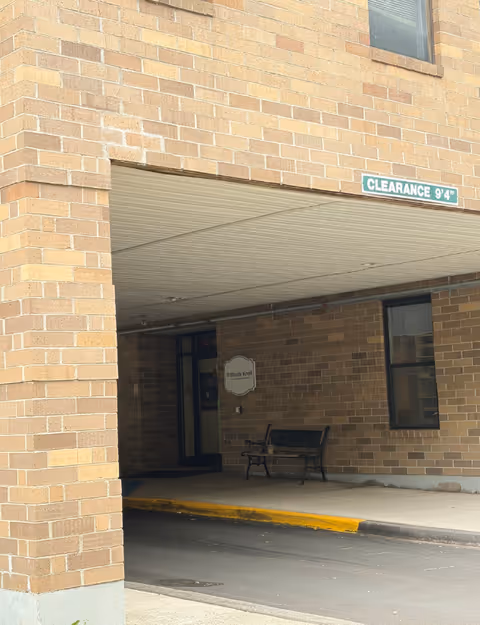 Brick building entrance under a canopy with a bench and Shady Knoll Health Center sign.