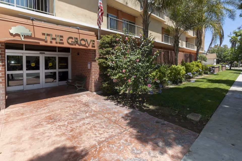 The Grove Care and Wellness entrance with glass doors, brick facade, walkway, and landscaping.