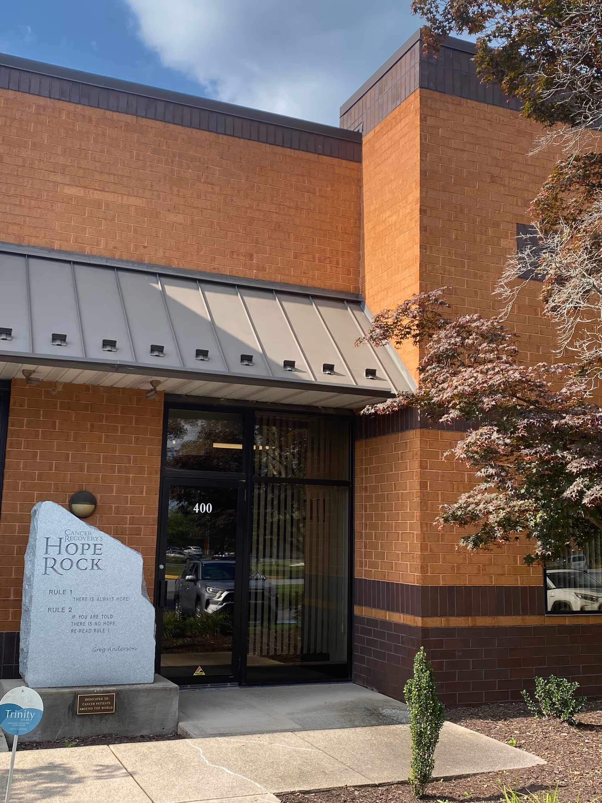 Brick building entrance with glass doors and a Hope Rock sign beside light landscaping.